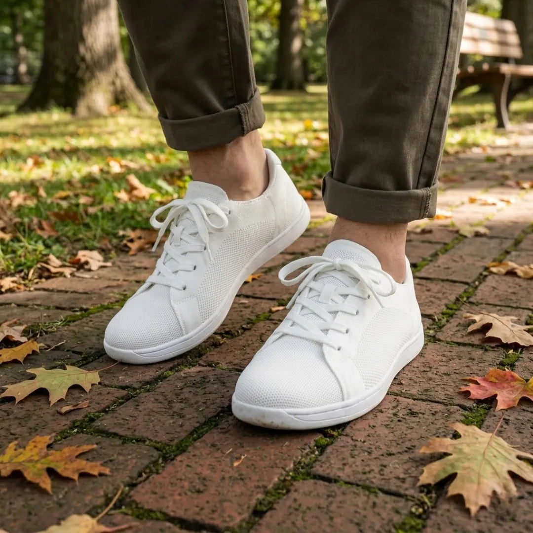 Person in olivgrüner Hose trägt die weißen Sneaker auf herbstlichem Backsteinweg mit buntem Laub im Park 38
