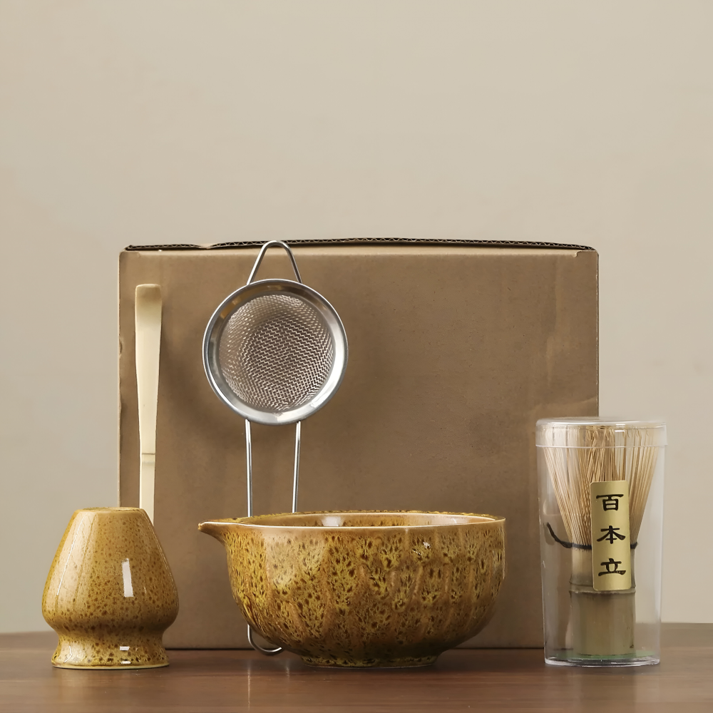 5-teiliges Matcha-Set in senfgelber, gesprenkelter Glasur vor einem braunen Versandkarton