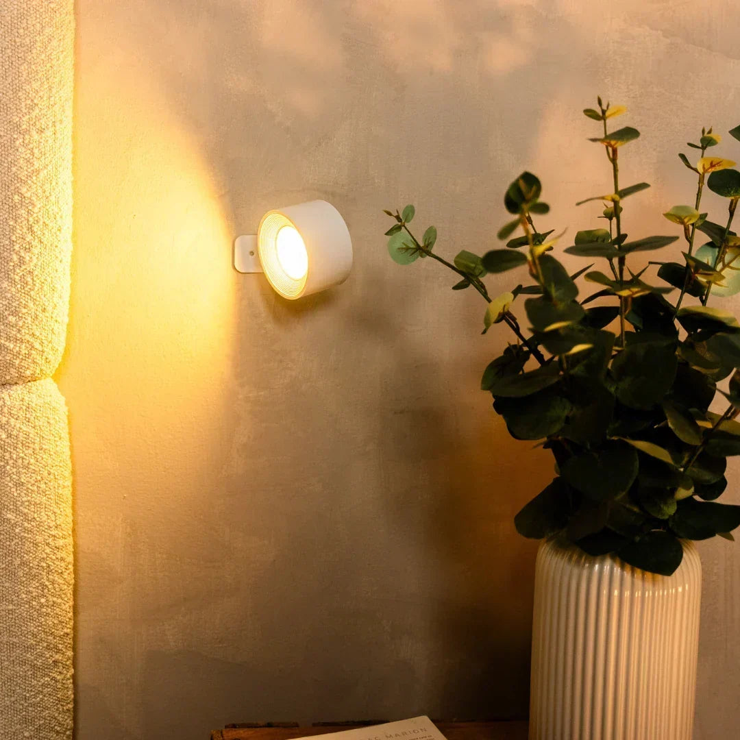 Weiße Wandleuchte strahlt warmes Licht neben einem Bouclé-Polster, daneben eine Vase mit Eukalyptus 6