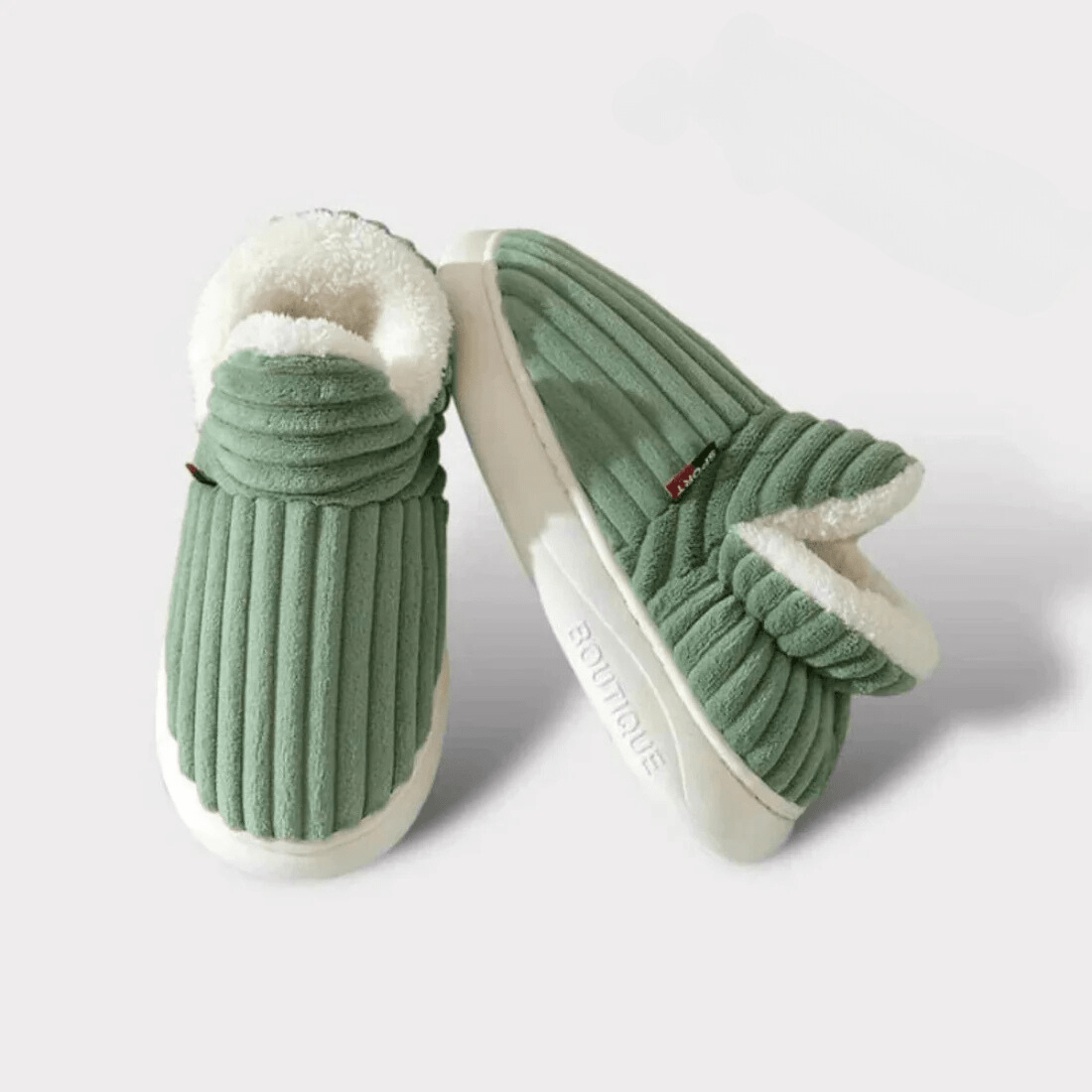 Grünes Paar gerippter Hausschuhe vor hellem Hintergrund, ein Schuh schräg aufgestellt, sodass die dicke weiße Sohle sichtbar ist.