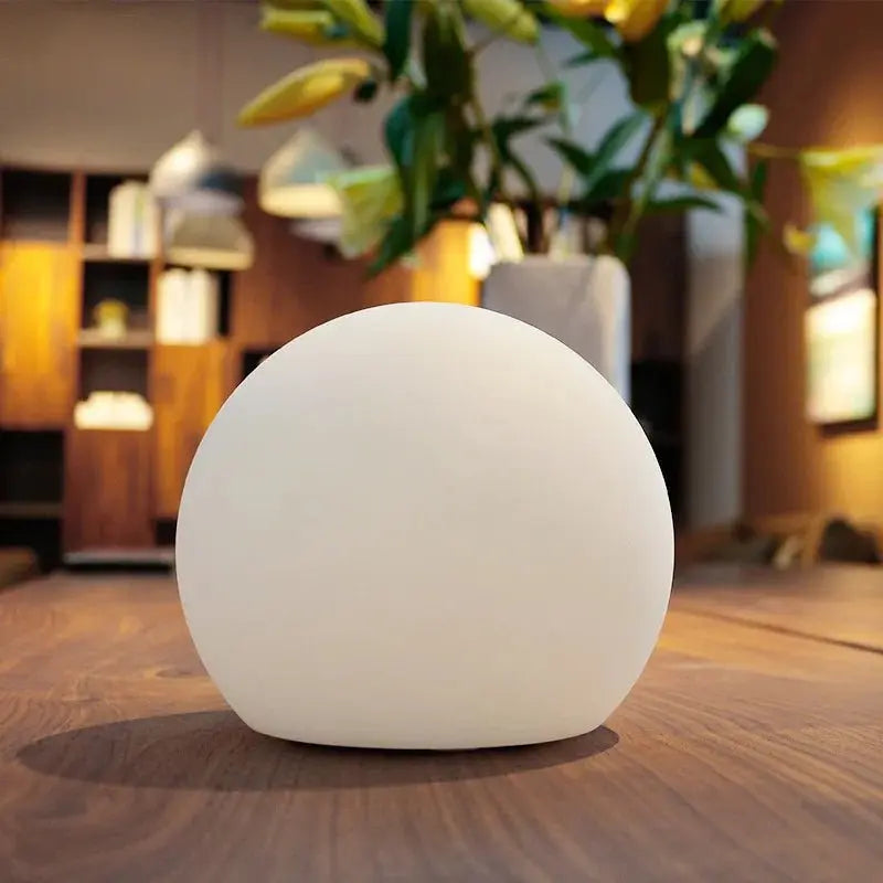 Ausgeschaltete weiße LED-Kugellampe auf einem Holztisch in einem Wohnraum mit Regal und Pflanze im Hintergrund.