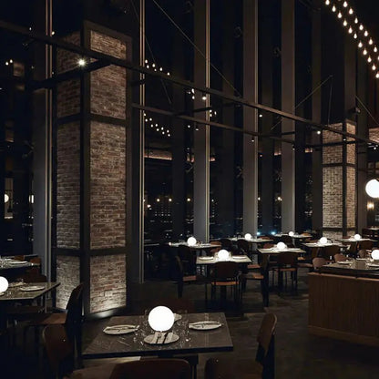 Mehrere leuchtende LED-Kugellampen auf den Tischen eines großen Restaurants mit Backsteinsäulen und Lichterketten.