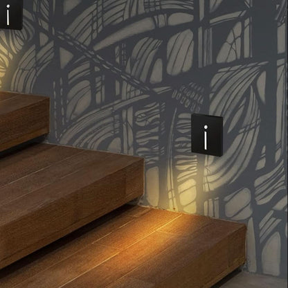 Schwarze Wandleuchten mit schmalem Lichtschlitz neben Holztreppe an gemusterter Wand, warmes Licht fällt auf die Stufen 2