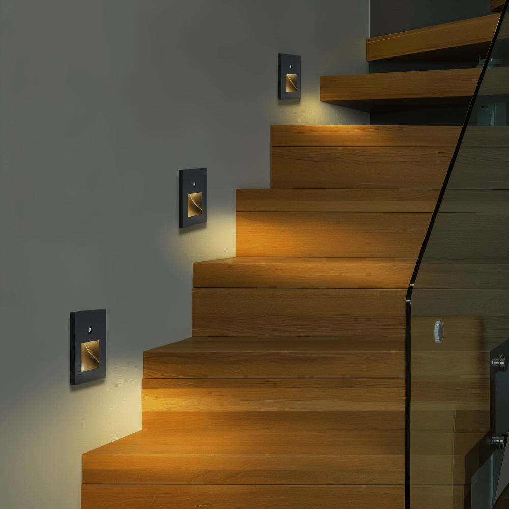 Dunkle quadratische Wandleuchten mit warmem Licht beleuchten eine Holztreppe mit Glasgeländer 3