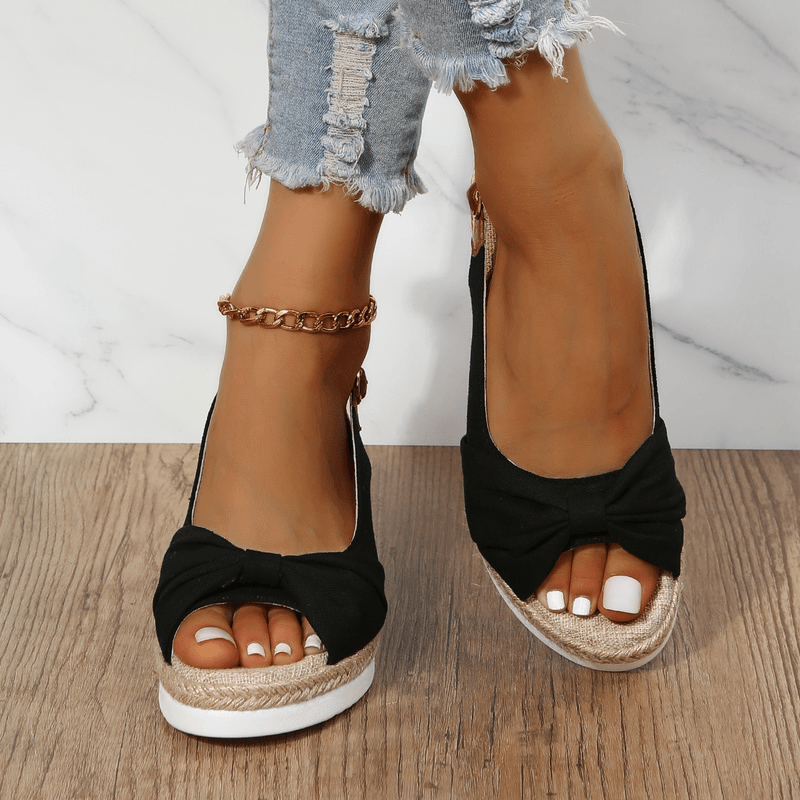 Schwarze Damen-Sandalen mit Keilabsatz, Schleife, bequem, Sommermode, auf Holzfußboden.