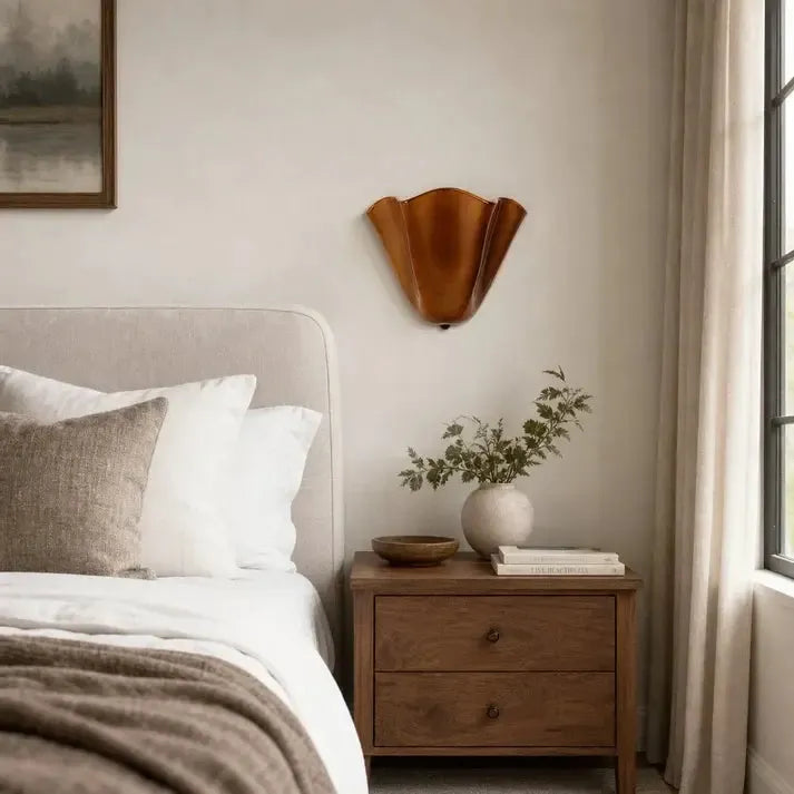 Bernsteinfarbene Wandlampe in Schalenform über einem Holznachttisch.