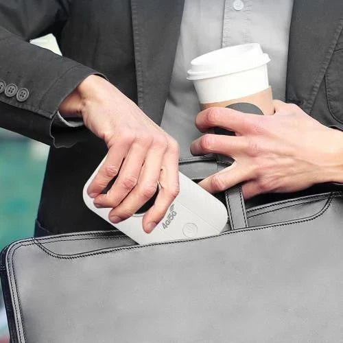 Mann steckt den kleinen weißen Router in eine graue Aktentasche, in der Hand einen Kaffeebecher 2