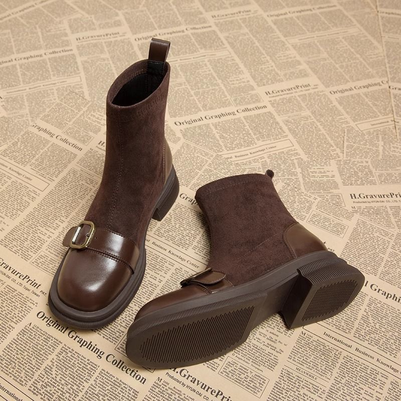Braune Wildlederstiefel mit Lederkappe und Schnalle, liegend mit sichtbarer profilierter Gummisohle und Blockabsatz.