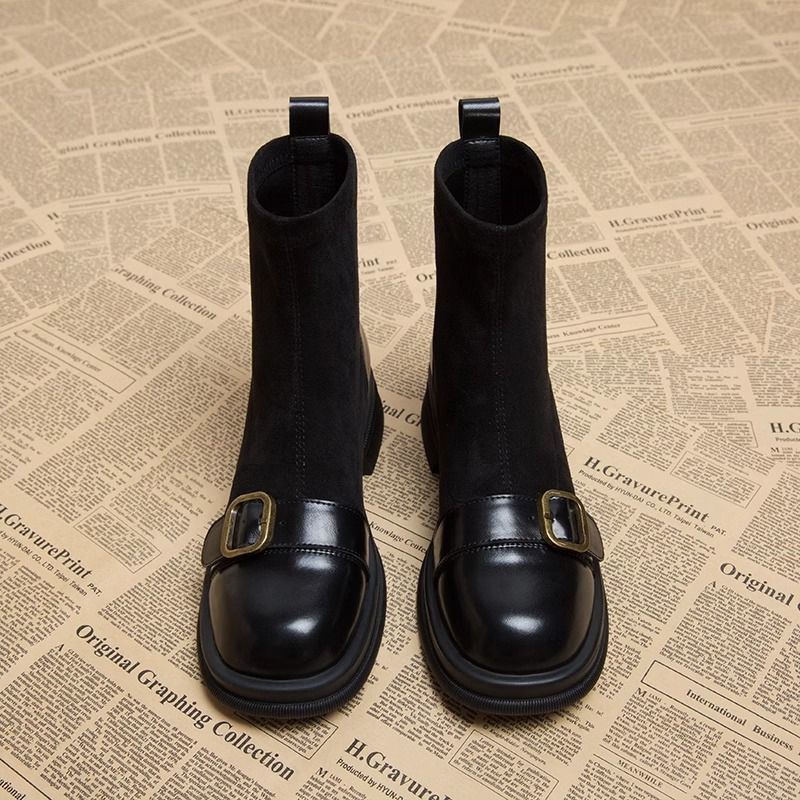 Schwarze Wildlederstiefel nebeneinander mit glänzender Lederkappe, goldfarbener Schnalle und runder Schuhspitze, weitere Ansicht.