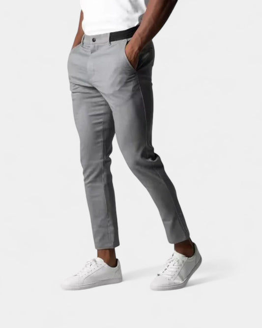 Model in grauer Slim-Tapered-Hose, weißem Shirt und weißen Sneakern, Hände in den Taschen, Seitenansicht 1