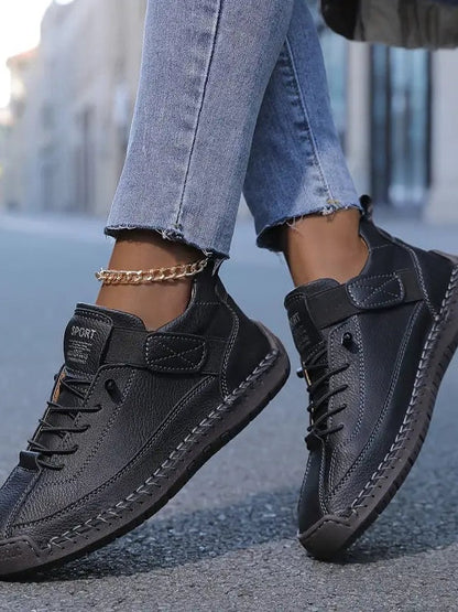 Schwarze Sneaker an den Füßen einer Frau mit goldener Fußkette, seitlich auf Asphalt fotografiert 5
