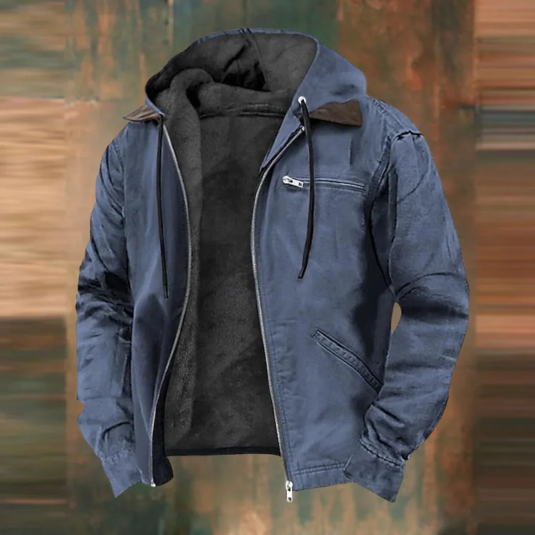 Die Jacke in Blaugrau, offen mit dunklem Fleecefutter vor unscharfem braun-grünem Hintergrund.