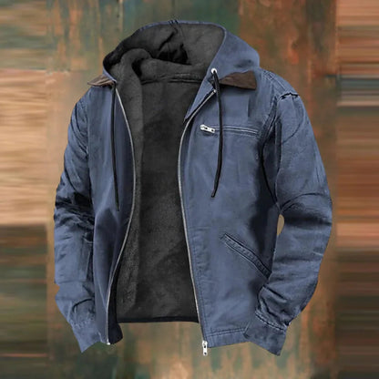 Die Jacke in Blaugrau, offen mit dunklem Fleecefutter vor unscharfem braun-grünem Hintergrund.