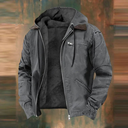 Die Jacke in Anthrazitgrau, offen mit Kapuze, Kordeln und dunklem Plüschfutter vor unscharfem Hintergrund.