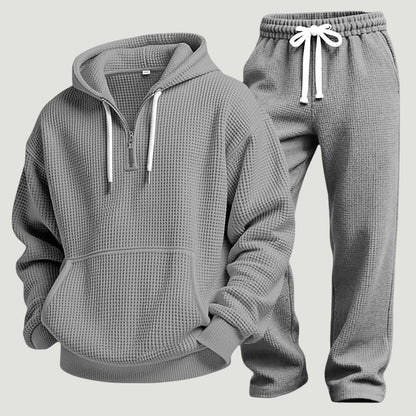 Graues Waffelstrick-Set aus Hoodie mit halbem Reißverschluss und Jogginghose mit weißem Kordelzug, freigestellt nebeneinander. 10