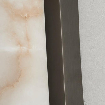Nahaufnahme der Marmoroberfläche mit zarten rosafarbenen Adern neben der gebürsteten, kantigen Metallhalterung an einer hellen Wand. 25