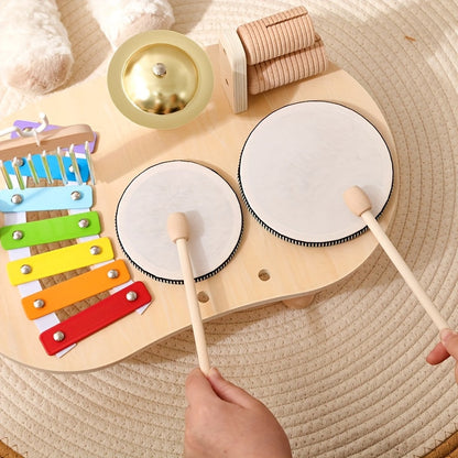 Draufsicht auf zwei Trommeln, auf die eine Hand mit zwei Holzschlägeln trommelt, links das bunte Xylophon, oben Becken und Rassel. 5