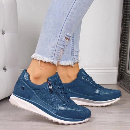 Getragener Sneaker in Blau mit seitlichem Reißverschluss, Schnürung und perforiertem Obermaterial, kombiniert mit heller, ausgefranster Jeans. 5