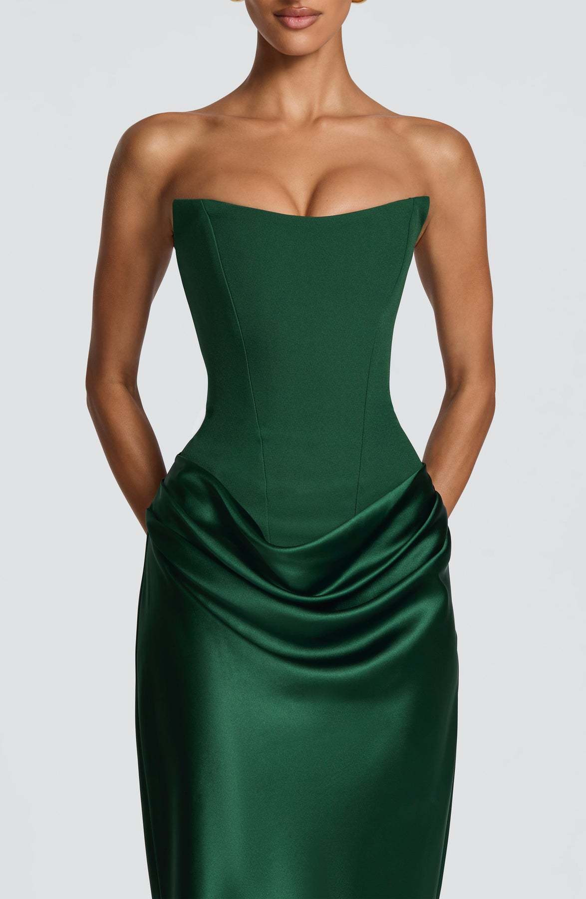 Nahaufnahme des grünen Korsettoberteils mit Nahtlinien und der Drapierung an der Hüfte, Hände in den Taschen 4