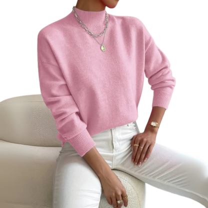 Damen Pullover in Rosa mit Polokragen und weißer Jeans, sitzend auf einem Bouclé-Sessel.