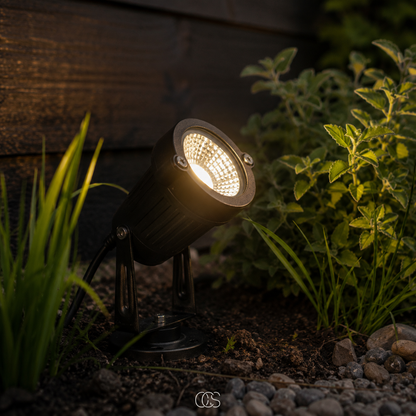 Schwarzer LED-Gartenstrahler mit Erdspieß aus Metall in Nahaufnahme, warmweiß leuchtend im Beet.
