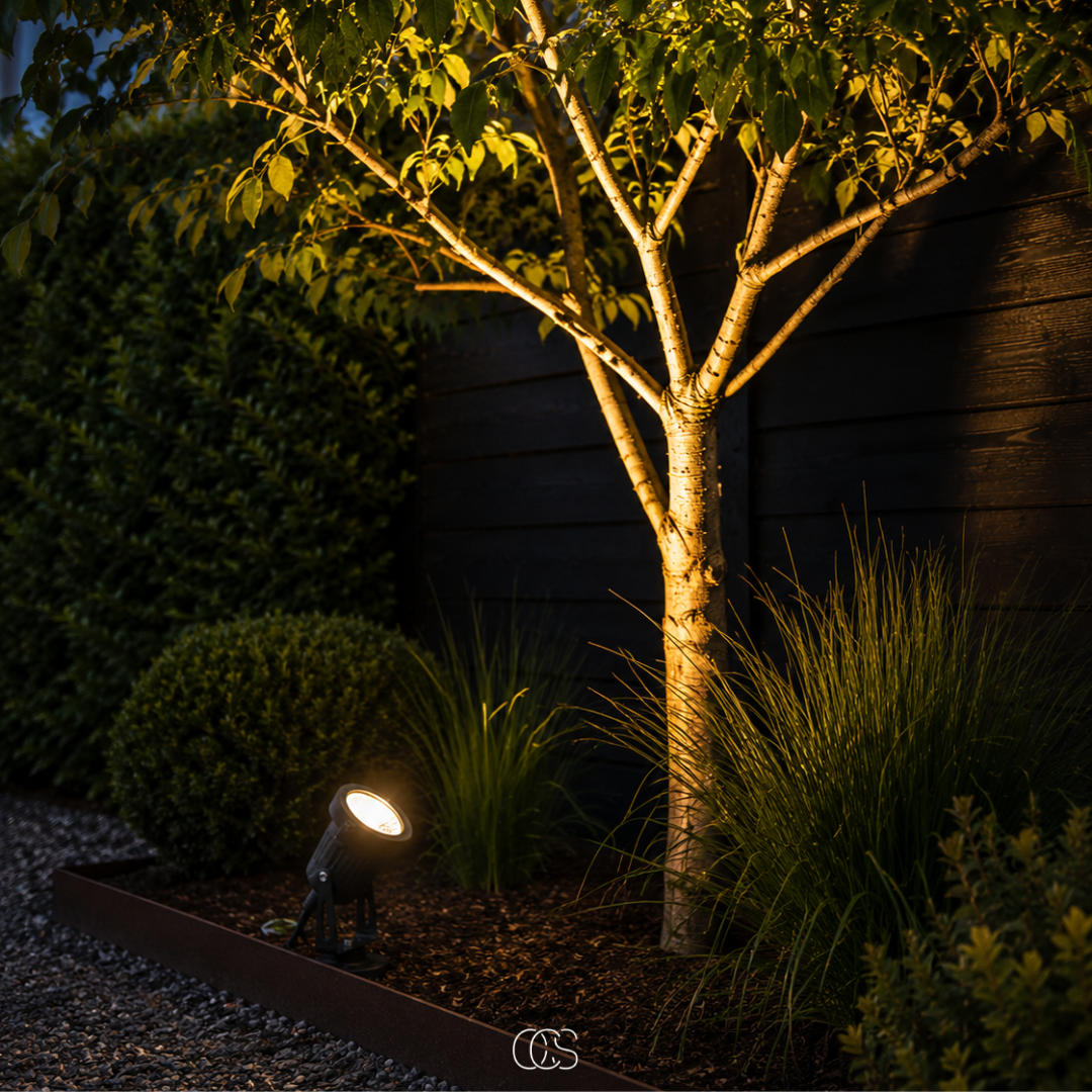 Schwarzer LED-Gartenstrahler mit Erdspieß aus Metall in detail beleuchtet den Stamm eines Baums.
