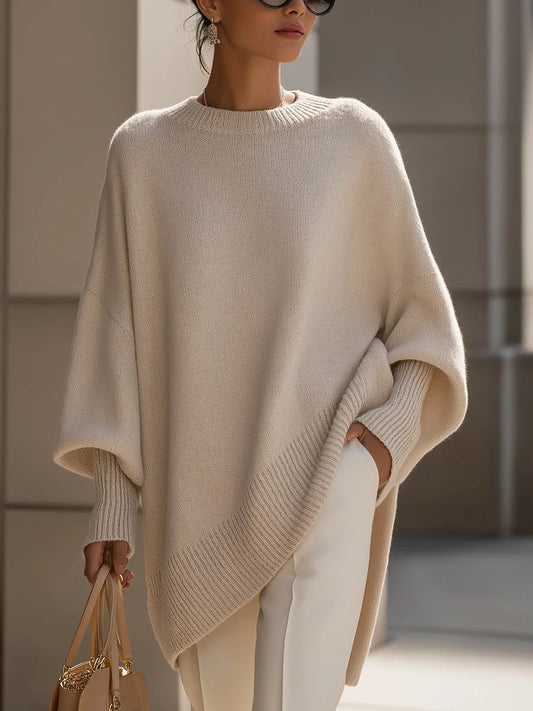 Beigefarbener Oversize-Strickpullover mit Rippsaum, von einem Model mit weißer Hose und heller Handtasche getragen, Vorderansicht. 1