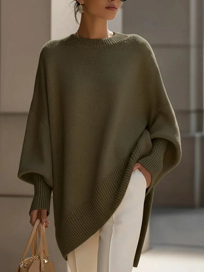 Oliv- bis moosgrüner Oversize-Pullover mit asymmetrischem Rippsaum, am Model mit weißer Hose und Handtasche, Vorderansicht. 7