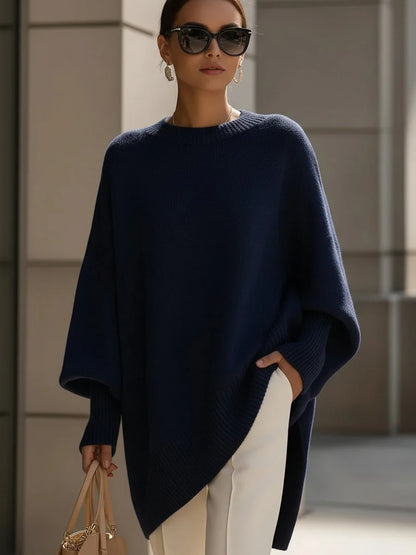 Dunkelblauer Oversize-Pullover mit weiten Ärmeln, am Model mit Sonnenbrille, weißer Hose und heller Handtasche. 8