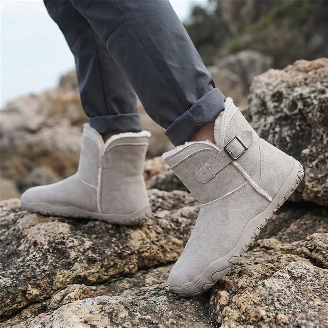 Beigegraue Stiefel an den Füßen eines Trägers in Jeans, der über Felsen am Meer geht 29