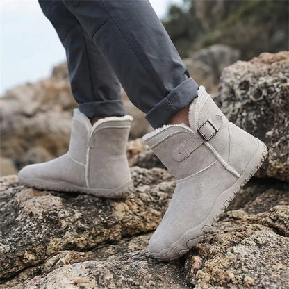 Beigegraue Stiefel an den Füßen eines Trägers in Jeans, der über Felsen am Meer geht 29