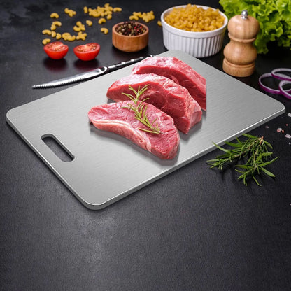 Edelstahl-Schneidebrett mit rohem Fleisch, Rosmarin, Gewürzen, Tomatenhälften, Nudeln und einem Messer.