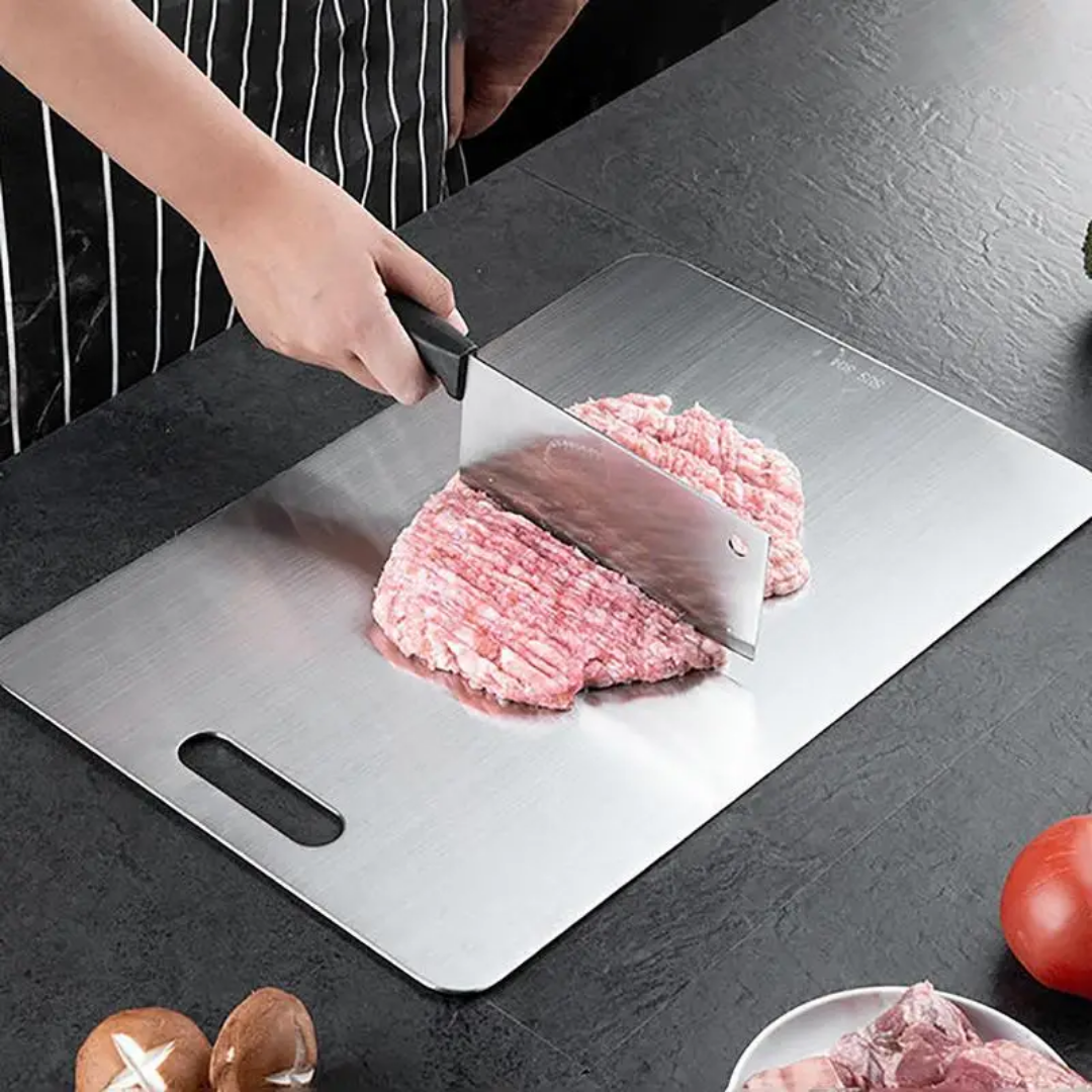 Edelstahl-Schneidebrett mit Hackmesser, Hackfleisch, Pilzen, Tomate und einer Schale mit Fleisch.