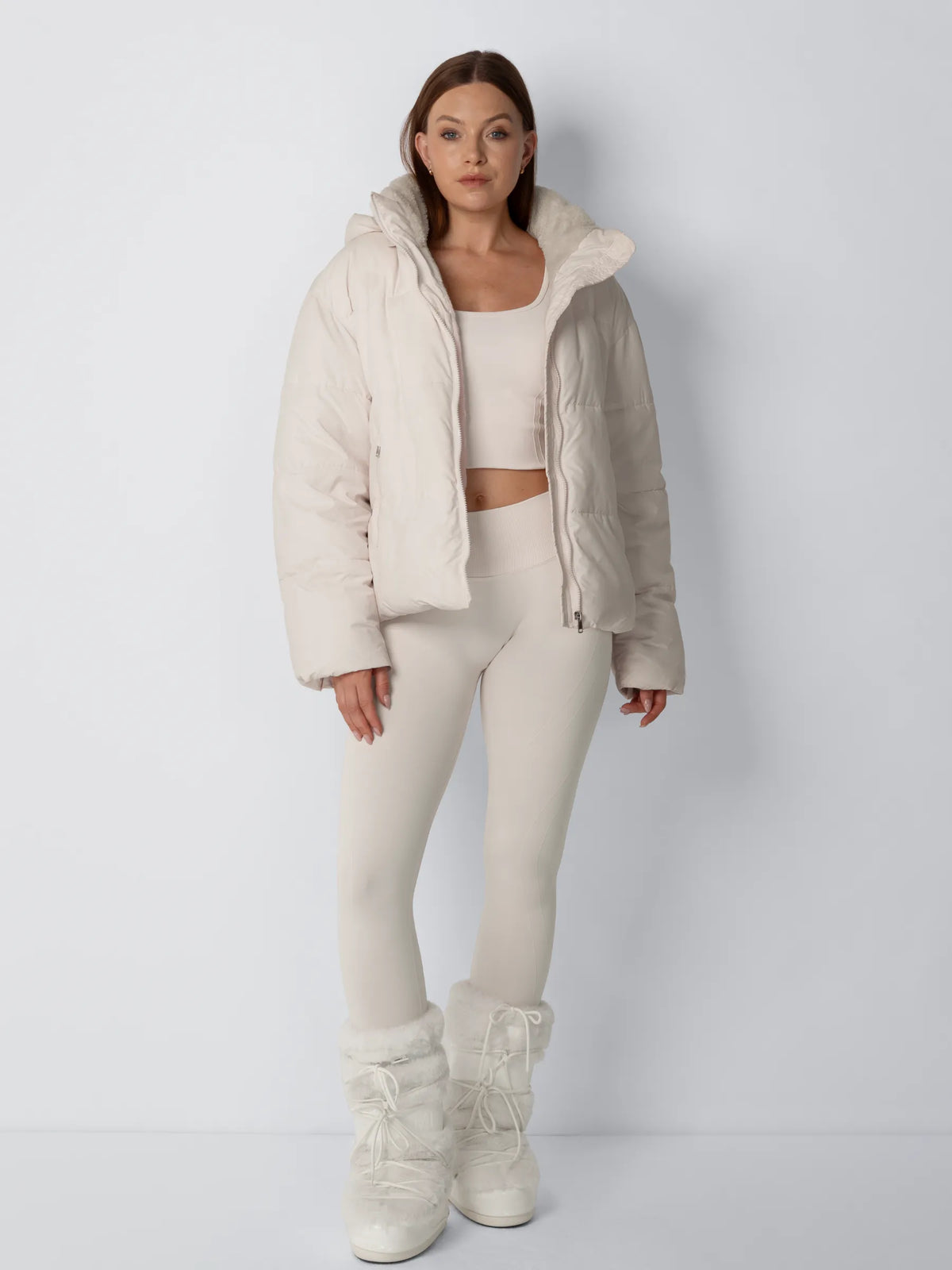 Ganzkörperansicht des Models in offener cremeweißer Steppjacke, hellem Set und weißen Fellstiefeln 5