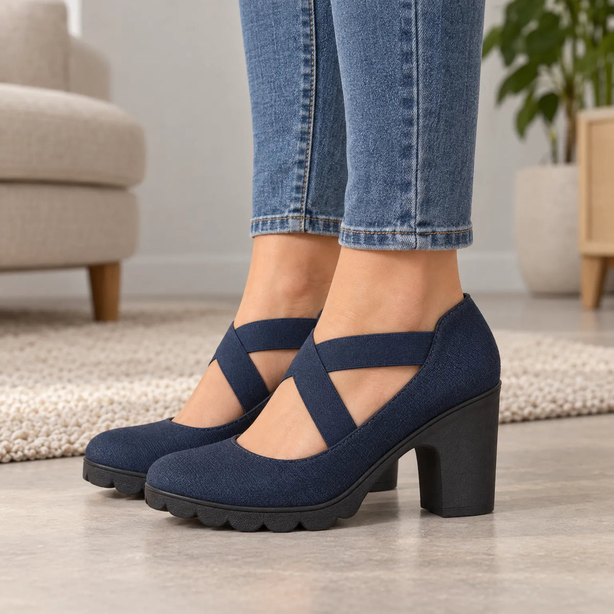 Nahaufnahme einer Frau in Jeans, die dunkelblaue Mary Janes mit gekreuzten Riemen, Blockabsatz und Profilsohle im Wohnzimmer trägt. 2
