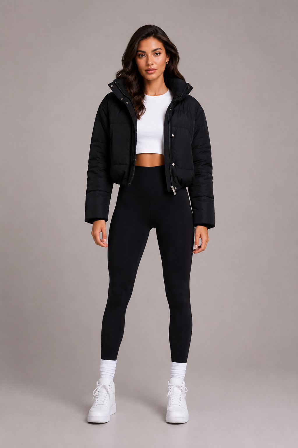 Schwarze kurze Steppjacke von vorn, offen getragen zu weißem Crop-Top, schwarzer Leggings und weißen Sneakern, 2