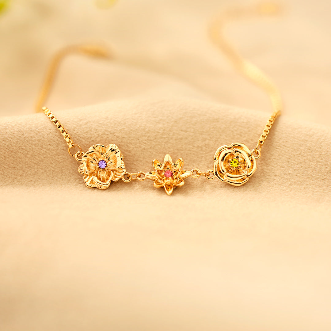 Goldene Blumenanhänger mit violettem, rosafarbenem und gelbgrünem Stein auf weichem beigem Stoff. 14