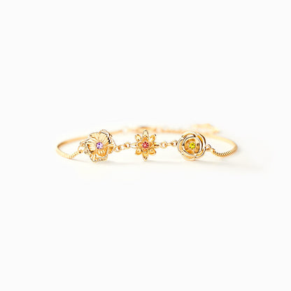 Goldenes Blumenarmband in Frontansicht auf hellem Hintergrund mit drei Blumenanhängern und farbigen Steinen. 4