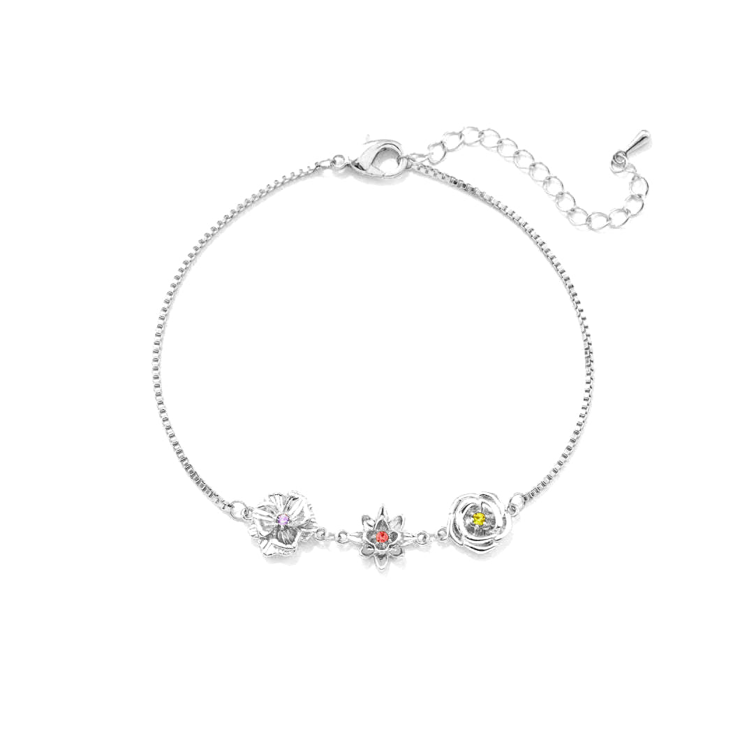 Silberfarbenes Armband mit drei Blumenanhängern und farbigen Steinen in der Mitte, von oben auf weißem Hintergrund. 2