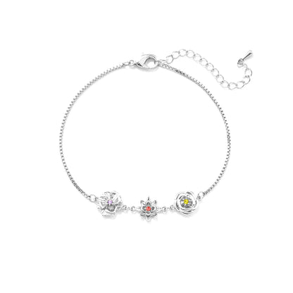 Silberfarbenes Armband mit drei Blumenanhängern und farbigen Steinen in der Mitte, von oben auf weißem Hintergrund. 2