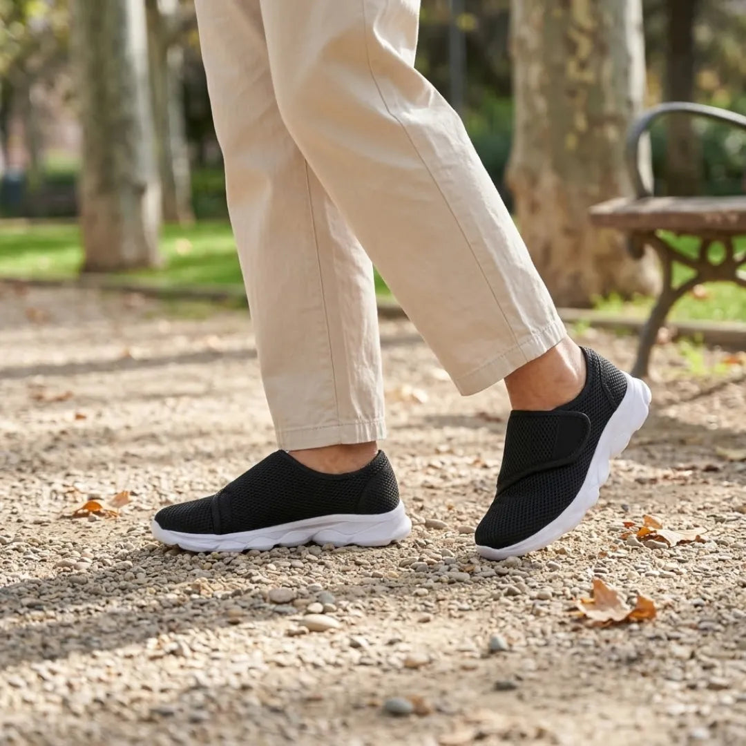 Person in beigen Hosen geht in schwarzen Netz-Schuhen mit Klettband und weißer Sohle über einen Kiesweg im Park. 20