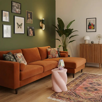 Wandlampe in Dunkelgrün und Creme an grüner Wand über einem orangefarbenen Ecksofa mit rosa Beistelltisch und gemustertem Teppich. 9
