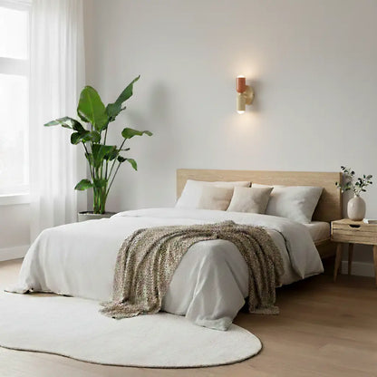 Kleine Wandlampe in Terrakotta und Creme über einem Doppelbett mit weißer Bettwäsche, Pflanze und rundem Teppich im hellen Schlafzimmer. 8