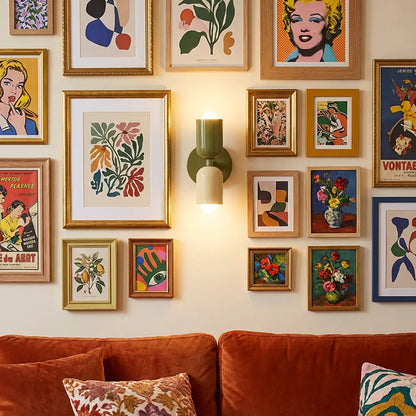 Wandlampe in Olivgrün und Creme inmitten einer dichten Galerie gerahmter Poster über einem orangefarbenen Samtsofa mit Kissen. 6
