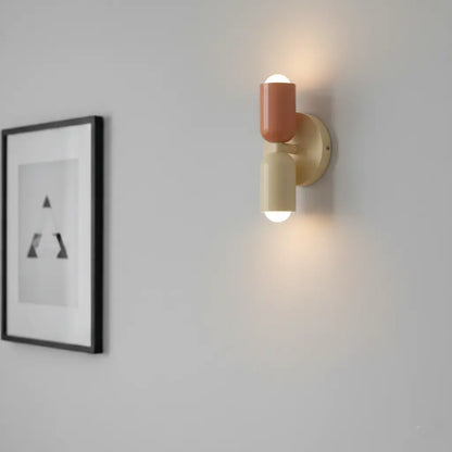 Eingeschaltete Wandlampe in Terrakotta und Creme mit rundem Wandteller, daneben ein schwarz gerahmtes Bild an hellgrauer Wand. 4