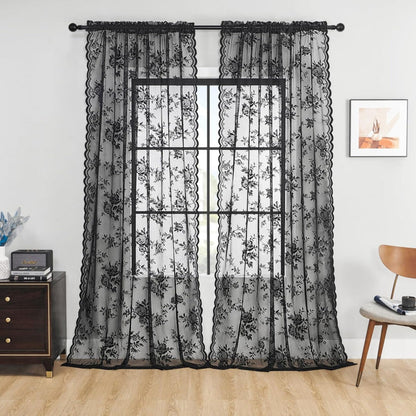 Zwei schwarze transparente Spitzenpaneele mit Rosenmuster und Wellenkante hängen an einer Stange vor einem Fenster in einem Wohnzimmer. 1