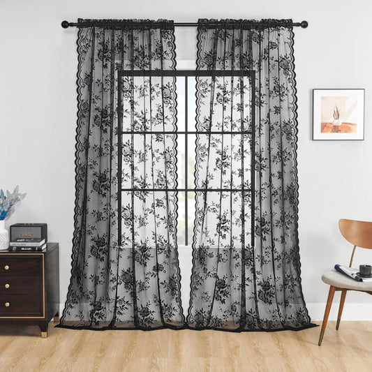 Zwei schwarze transparente Spitzenpaneele mit Rosenmuster und Wellenkante hängen an einer Stange vor einem Fenster in einem Wohnzimmer. 1
