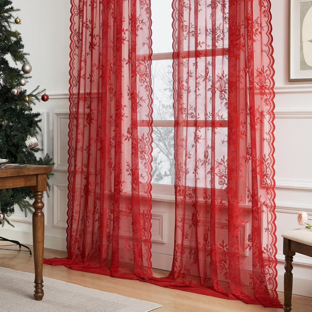 Zwei rote transparente Spitzenvorhänge mit Rosenmuster und gewellten Kanten vor einem Fenster, daneben ein Weihnachtsbaum und ein Holztisch. 7