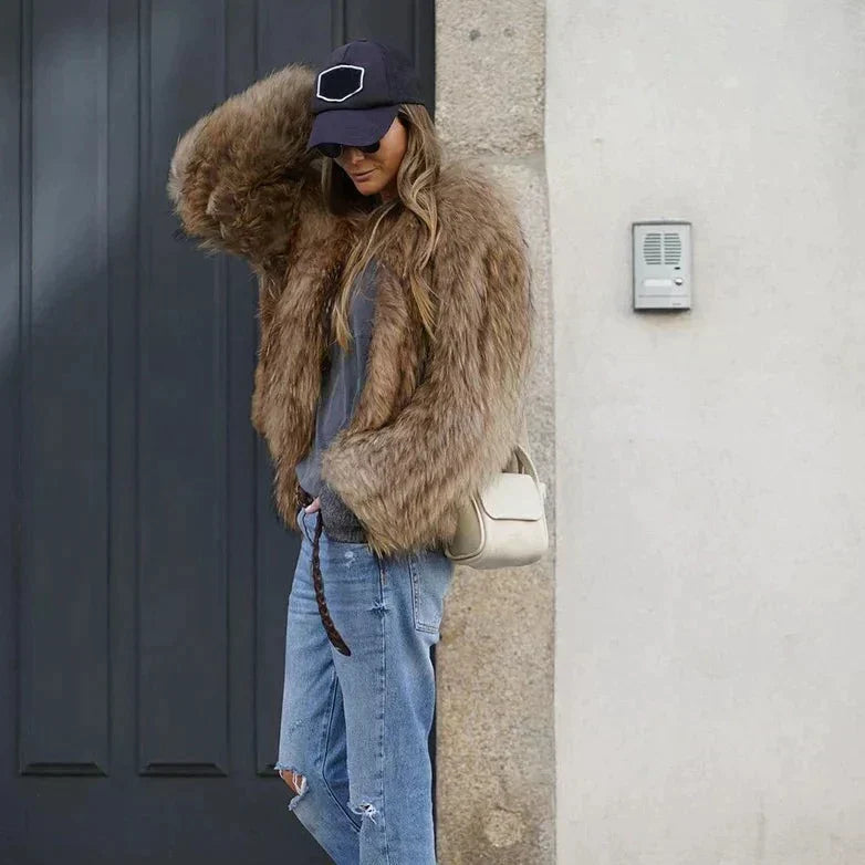 Frau in brauner Kunstpelzjacke, zerrissene Jeans, schwarze Kappe, weiße Tasche, urbaner Hintergrund.