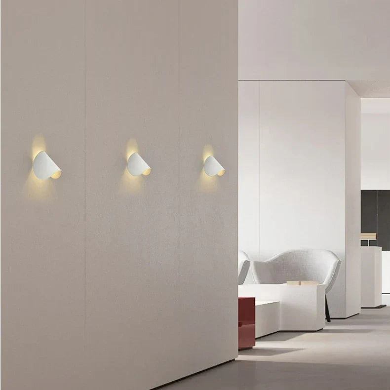 Drei weiße Wandleuchten in einer Reihe an einer Wand in einem hellen, modernen Raum.